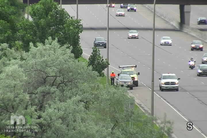 A worker in an orange vest stands by a vehicle on the shoulder of the highway.