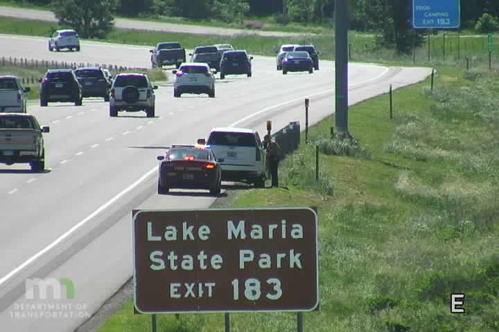 Police car and person on shoulder near Lake Maria State Park exit.