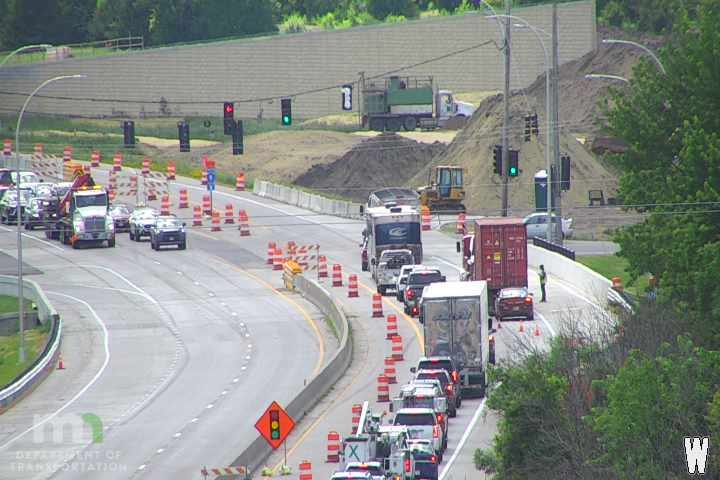 A person stands by a car in a construction zone with traffic cones and barriers.