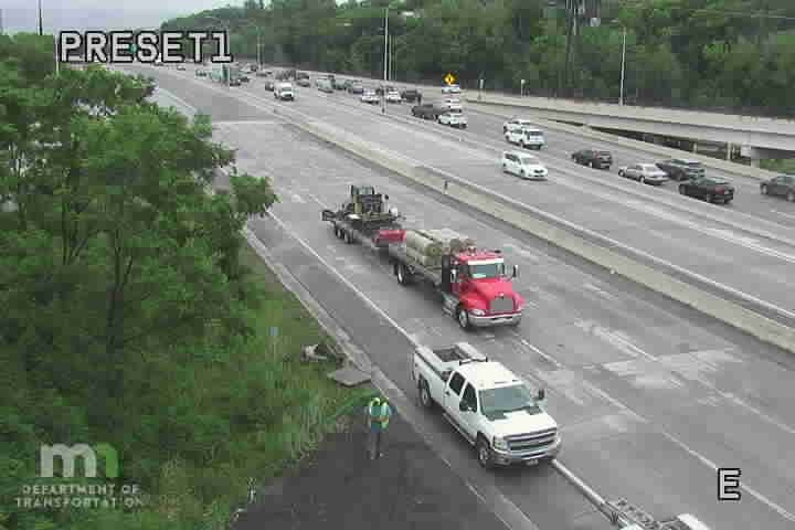 Worker in reflective vest near white pickup truck on highway shoulder.