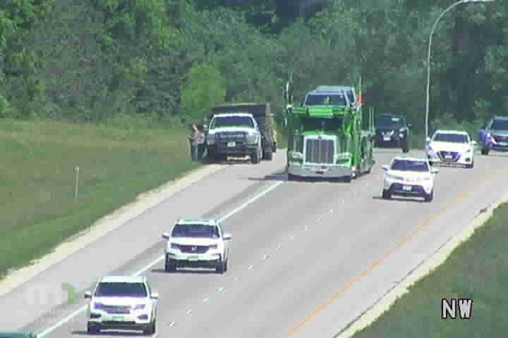 A white truck is stopped on the shoulder with a person standing next to it.