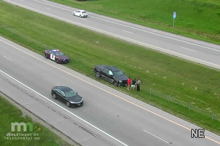 Police car with lights on the shoulder next to a black pickup truck with people standing nearby