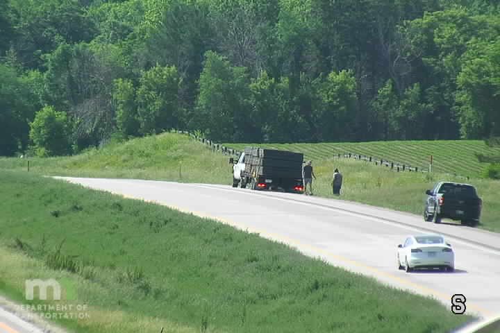 Two people standing by a truck on the shoulder of the road.