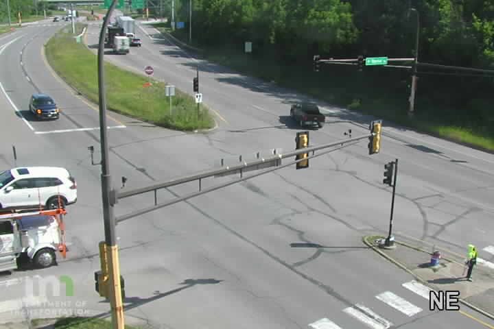A person in a high-visibility vest stands near a traffic signal.
