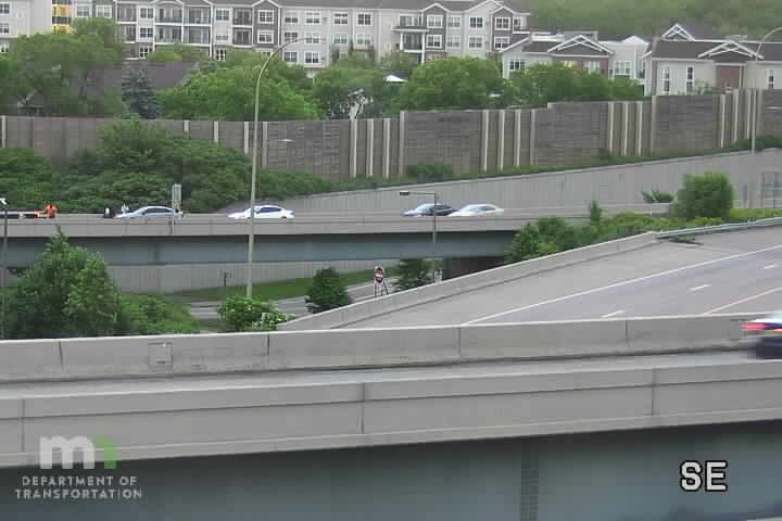 Two people in orange vests are attending to a stopped vehicle on the highway.