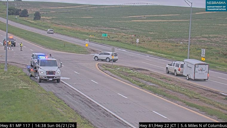 Tow truck with flashing lights and two individuals standing near it on the left shoulder