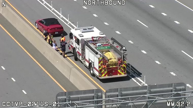 Fire truck and personnel on scene assisting with a stopped vehicle on the highway.