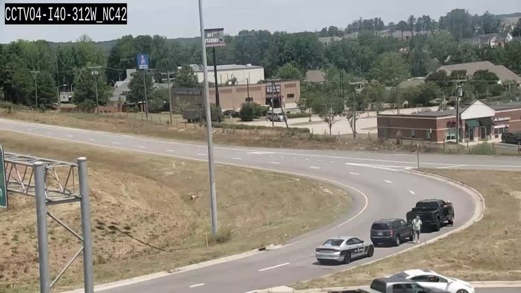 Police car and truck stopped on the side of the road with people present.