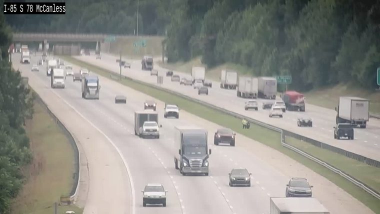 Person in yellow vest on shoulder of highway near traffic.
