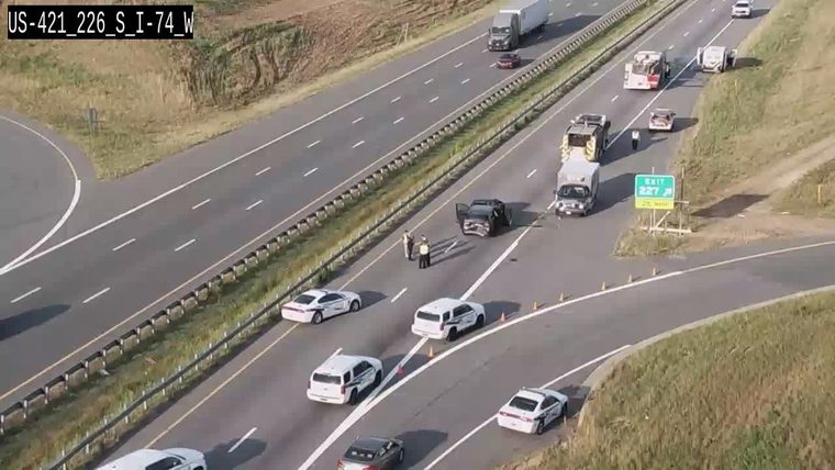 Multiple police vehicles and personnel at a roadside incident with a damaged car.