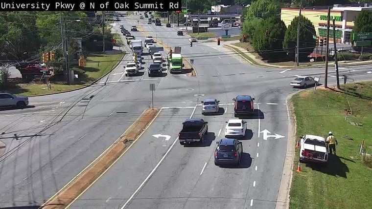 A person in a safety vest is near a white vehicle on the shoulder.