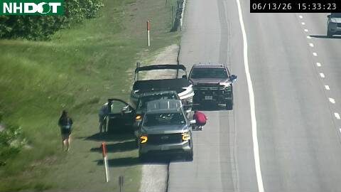 Two people and a vehicle are stopped on the shoulder, one person appears to be attending to something on the ground.