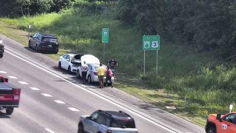 Two vehicles stopped on shoulder with people and a person in a safety vest.