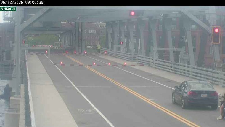 Person in high-visibility vest on bridge, traffic stopped by barriers.