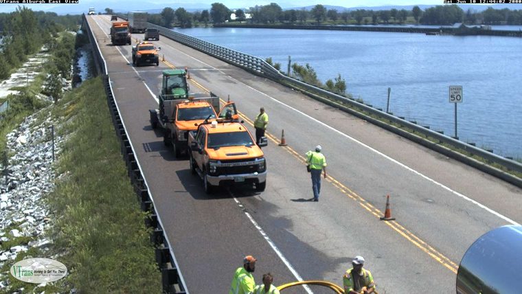 Road crew working on the bridge with cones and vehicles present.
