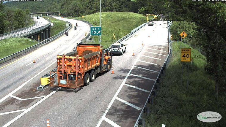 Road work with dump truck, cones, and construction equipment on ramp.