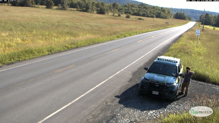 State Police vehicle with a person standing next to it on the right shoulder