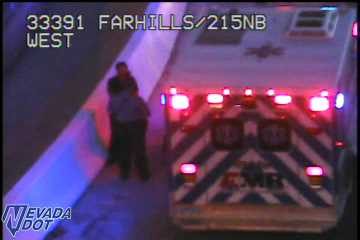 Ambulance with hazard lights on and two people standing next to it on the right shoulder
