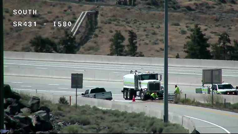 Pickup truck partially in ditch, with a large truck and two workers attending to it, and a police vehicle with lights on nearby.