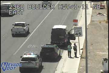 Police car with lights on behind a stopped SUV and van on the right shoulder, with two people standing outside