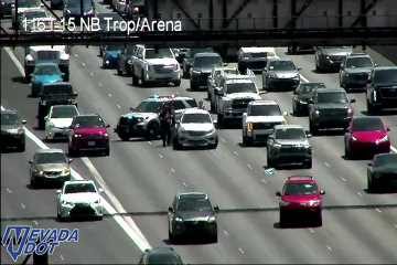 Police vehicle with emergency lights on and two people standing in the travel lane next to a white sedan