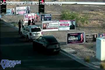 White SUV parked on the right shoulder with several people standing nearby on the sidewalk