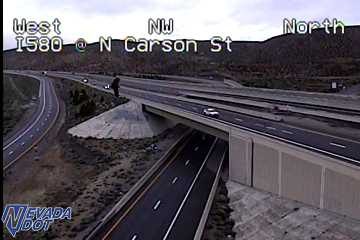 Pedestrian standing on the dirt shoulder near the bridge abutment on the left side of the highway