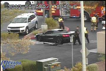 Fire truck with red and blue lights on, and multiple people in high-visibility vests near a black sports car