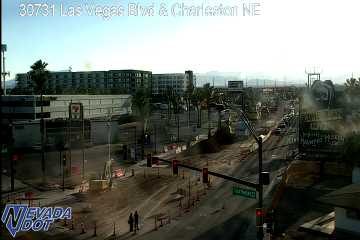 Construction zone with cones, barricades, and torn-up roadway blocking lanes, with two pedestrians walking in the foreground