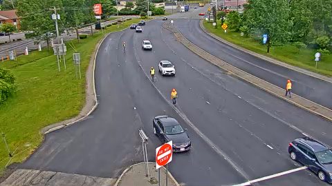 Workers in orange vests are present on the roadway, directing traffic.