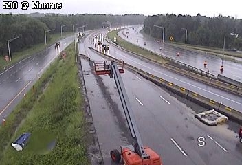 Construction lift and personnel on highway shoulder during rainy conditions.