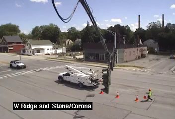 Utility truck and worker with cones on roadway, near traffic signal.