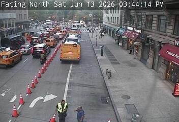 Two people in safety vests appear to be directing traffic around cones on-road cones.