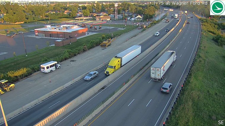 A white bus is stopped on the shoulder with cones nearby, possibly indicating an incident.