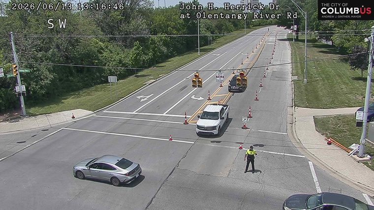 A police officer is directing traffic at an intersection with cones and temporary lane closures.