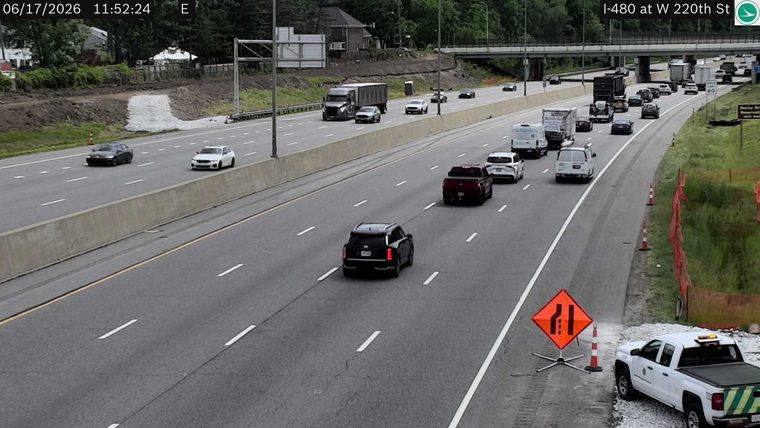 White pickup truck with flashing lights and cones on the shoulder, shoulder indicates road work or incident response.