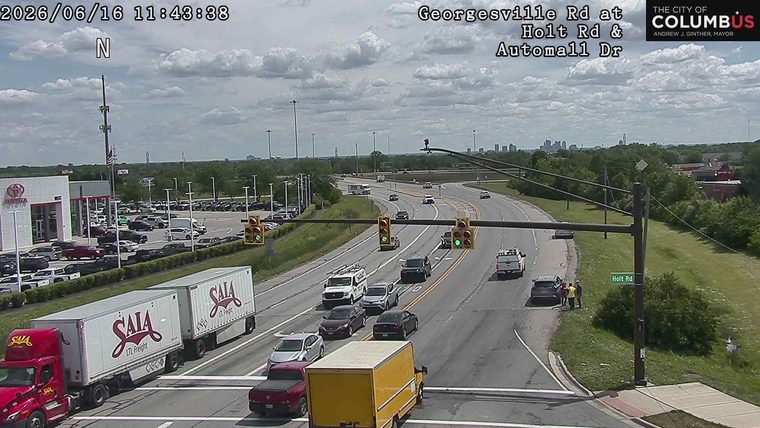 Two individuals in yellow vests appear to be responding to a vehicle on the shoulder.