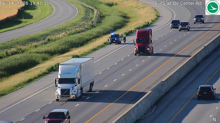 Police car and officer on the shoulder with a red semi-truck nearby.