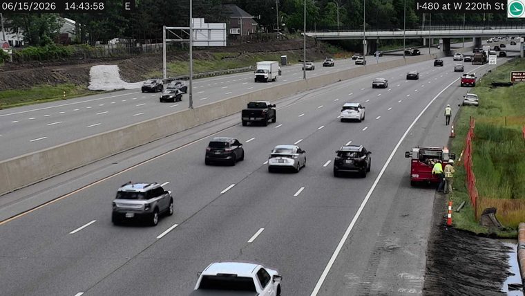 Two workers and a red truck are on the shoulder of the highway.