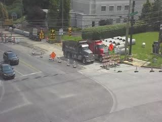Construction zone with trucks and equipment, traffic cones, and barriers present personnel present.