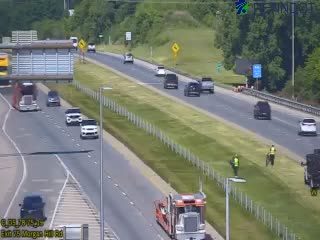 Two people in safety vests near a tow truck on the shoulder of the highway.