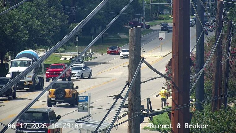Worker in reflective vest cleaning near roadside with a broom on the side of the road.