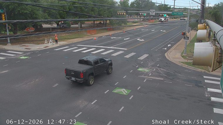 Person in orange vest and cones on sidewalk near intersection.