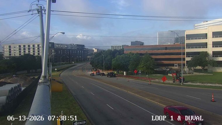 Construction zone with cones, barriers, and a small excavator on the side of the road.