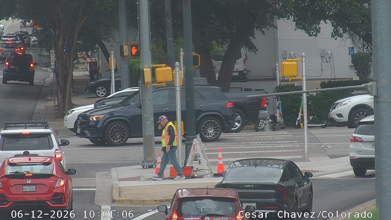Worker in reflective vest with cones and equipment on roadside.