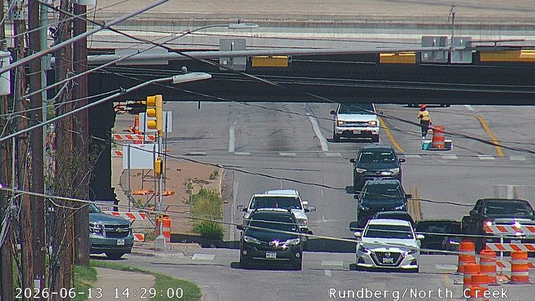Person in orange vest and hard hat directing traffic with cones.
