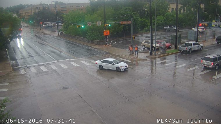 Two workers in orange vests are standing near a traffic signal.