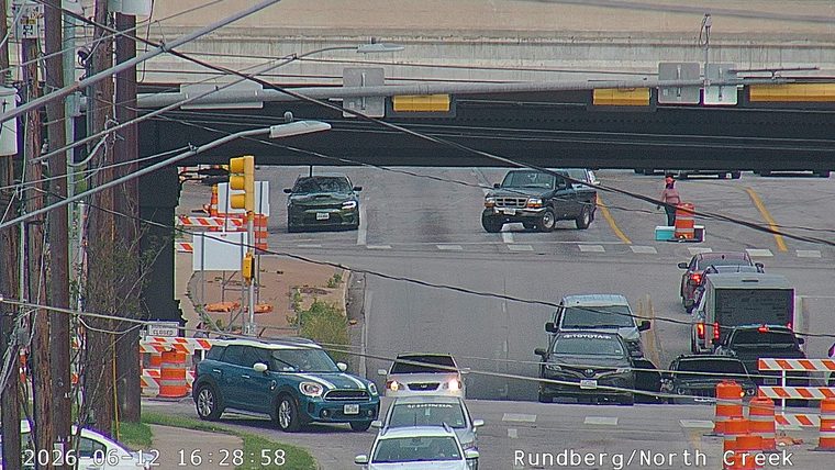 Person in orange vest directing traffic around cones and placing cones.