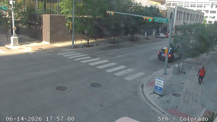 Police car with lights on at intersection, person walking on sidewalk.