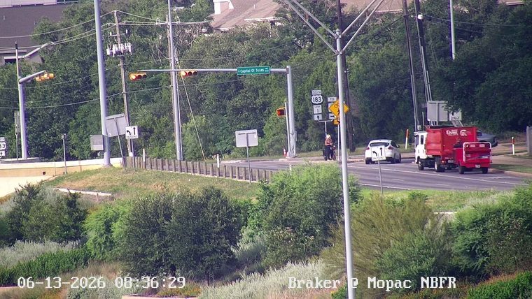 A person in a wheelchair is on the side of the road near a traffic light.